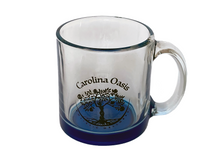 Load image into Gallery viewer, A clear, glass mug is featured with a blue base and the Carolina Oasis logo.
